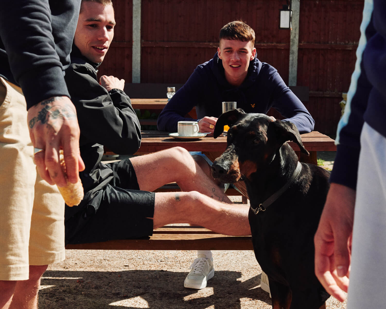 lads feed dog in pub beer garden by Tim Cole