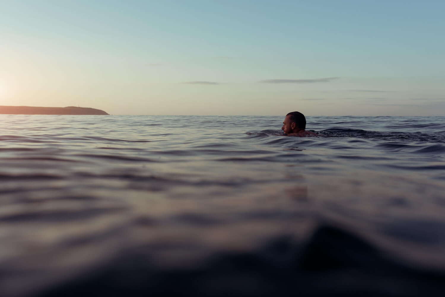 man swims towards sun at dawn in Carylon Bay Cornwall