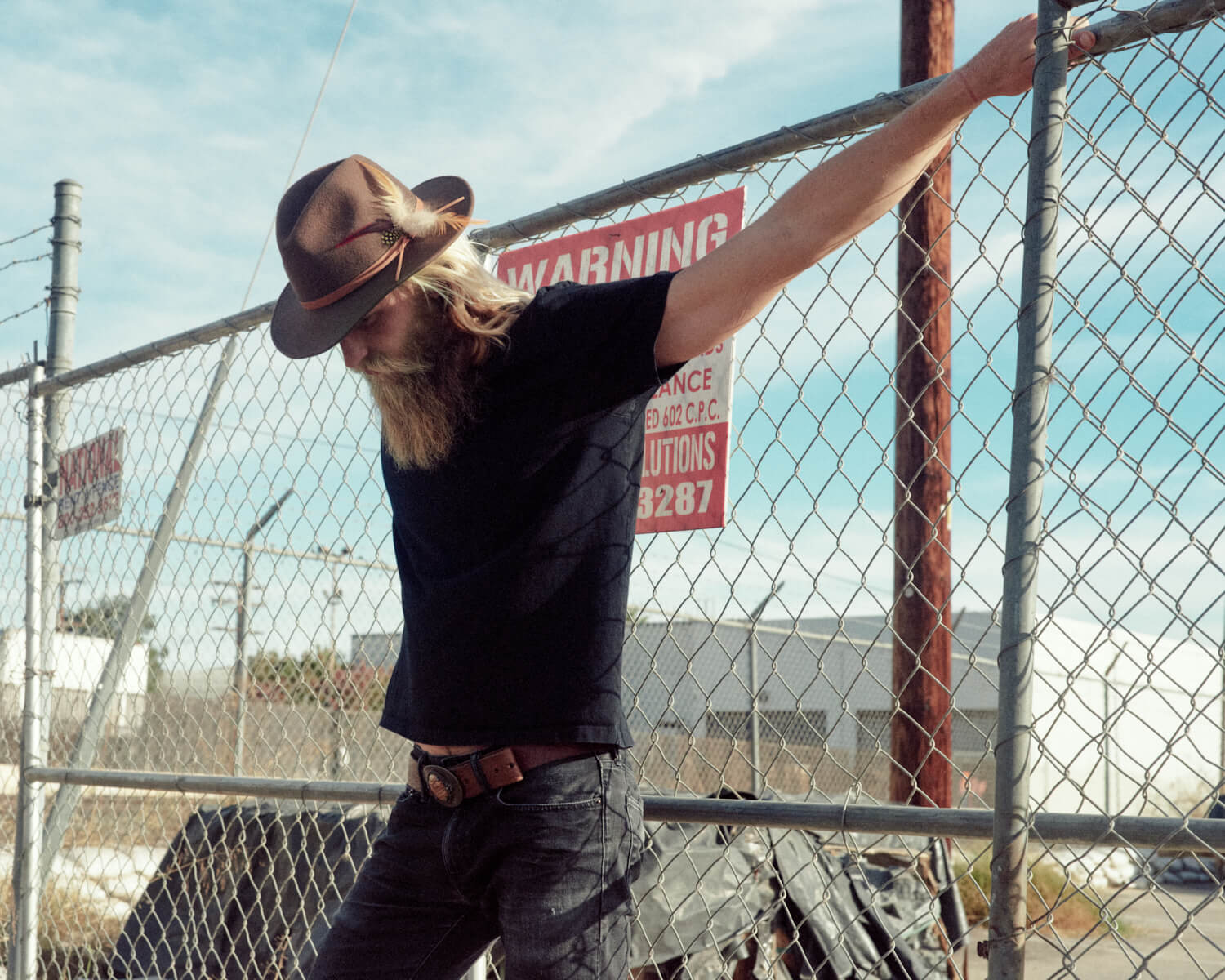 hipster hangs off wired gate by lifestyle photographer Tim Cole